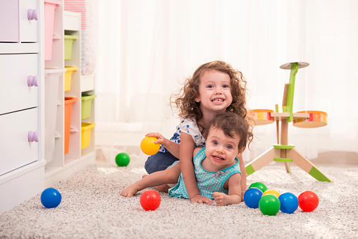 Two sister girls baby playing at playroom. Drum and colourful balls are on the background.
