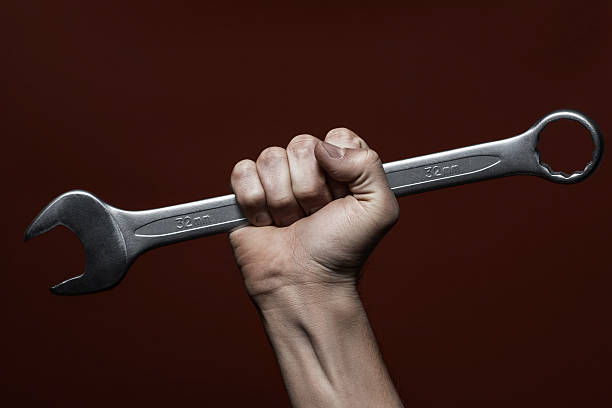 istock Male hand holding wrench, red background 596378556