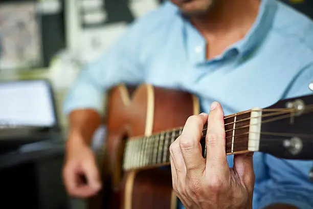 Midsection of man playing acoustic guitar at home