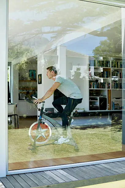 Full length side view of man working out on exercise bike at home
