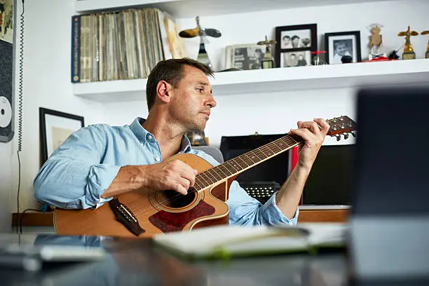 Mid adult man playing guitar at home