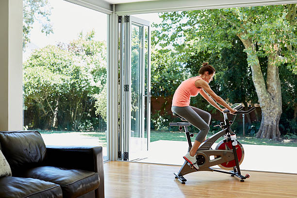 mujer haciendo ejercicio en bicicleta estática en casa - bicicleta estática fotografías e imágenes de stock