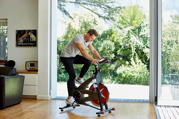 Man working out on exercise bike at home Full length of man working out on exercise bike at home peloton exercise bike stock pictures, royalty-free photos & images
