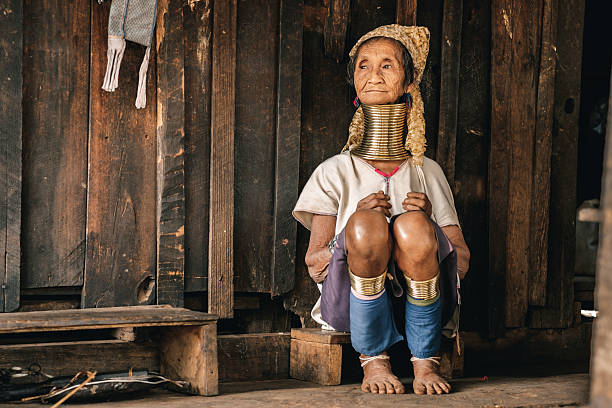 Traditional Padaung (Karen) woman from Myanmar Pan Pet, Myanmar - May 25, 2016: Portrait of Padaung (Karen) long neck woman in brass rings around their neck and traditional clothing near the house. Kayan tribe or Padaung are one of unique diverse ethnic minorities of east part of the country. Woman of the tribe are wearing a coil of brass rings around their necks from early age. Neck rings are very heavy. That is why collarbones and ribs goes down and starts deformation. There is  only visual  illusion of an elongated neck. For a long period of time Padaung people were persecuted by military regime over these visible tribal symbols. Some of them moved closer to the Thai border. But now situation has changed. The territory that  long time was restricted for tourist in Myanmar starts to be opened. padaung tribe stock pictures, royalty-free photos & images
