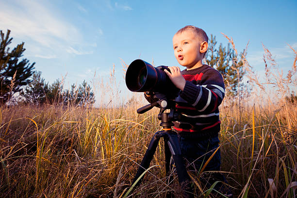 Beautiful smiling kid boy holding a DSLR camera in grass
