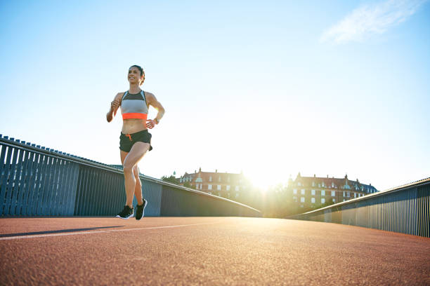 istock Low angle of sun behind woman running along bridge 596771506