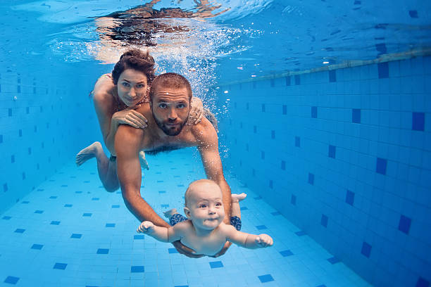 family fun in swimming pool. mother, father, baby dive underwater - baby swim under water bildbanksfoton och bilder