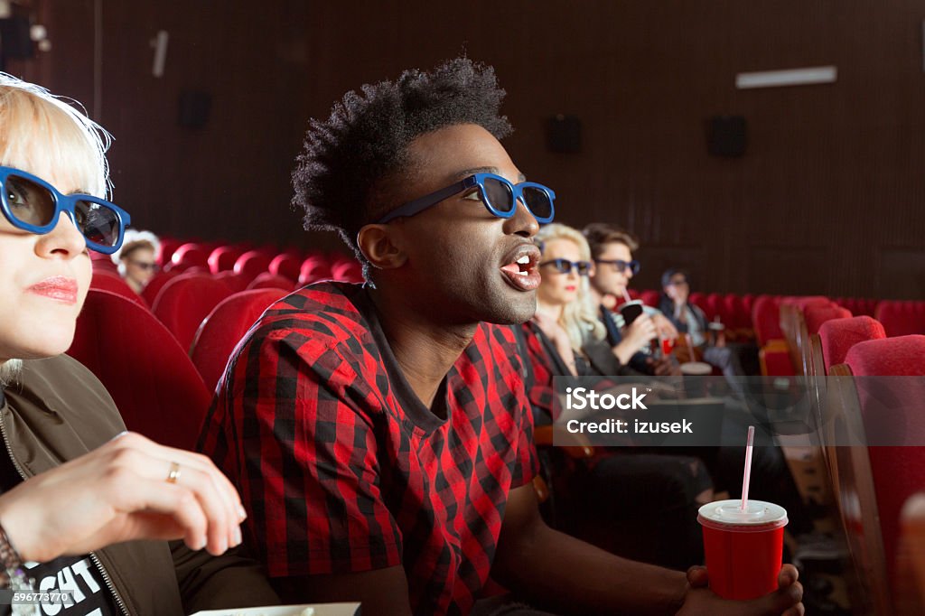 Young people in 3D movie theater Multi ethnic group of young adult people wearing 3D glasses, sitting in the cinema and watching 3D movie. Focus on afro american young man. Movie Theater Stock Photo