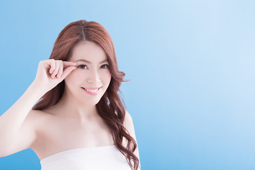 Woman face and eye care and she touch eye with hands, asian beauty. Isolated over blue background, asian beauty