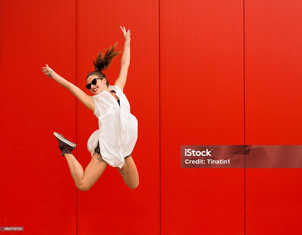 Active happy woman Stylish woman dancing and jumping on a street agains a red wall Red Stock Photo