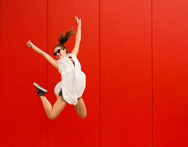 Stylish woman dancing and jumping on a street agains a red wall
