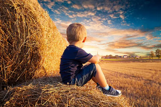 Baby sitting on bales of straw and looks up into the sunset