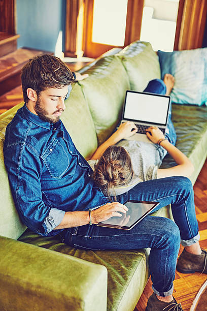 istock Young couple using digital tablet and laptop on sofa 596778550