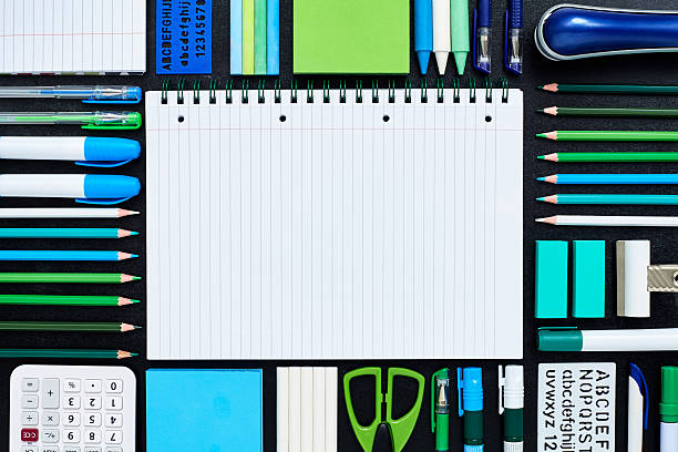Spiral notepad surrounded by school supplies on blackboard