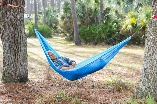 A senior African American woman sound asleep in a hammock between two trees.