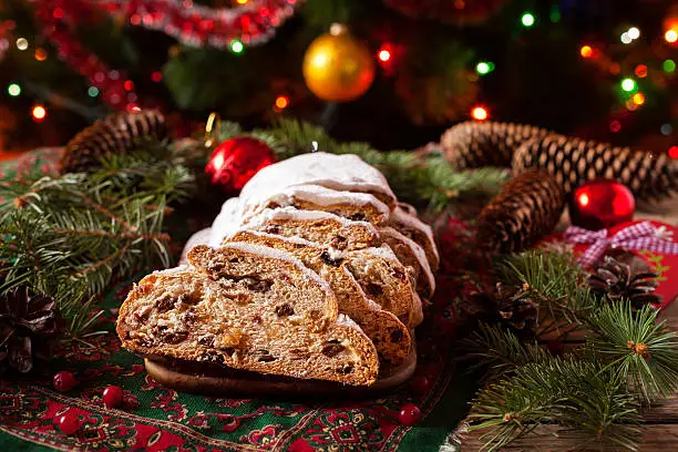Traditional German Dresdner Christmas cake Stollen with Berries and Nuts Raising on a rustic wooden festive table. Holiday xmas celebration baking fruitcake. Atmospheric, cozy, romantic decorations.