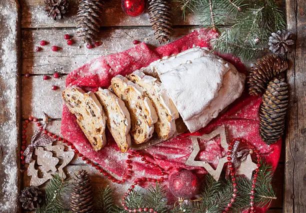 Traditional Dresdner German Christmas cake Stollen with Marzipan, Berries Nuts, Cinnamon, Raising on a rustic wooden festive table. Holiday xmas celebration decorations.