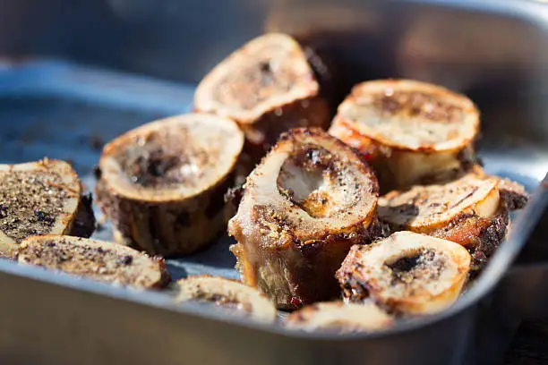 A horizontal composition of a roasting tray full of roasted beef marrow bones grilled to golden perfection