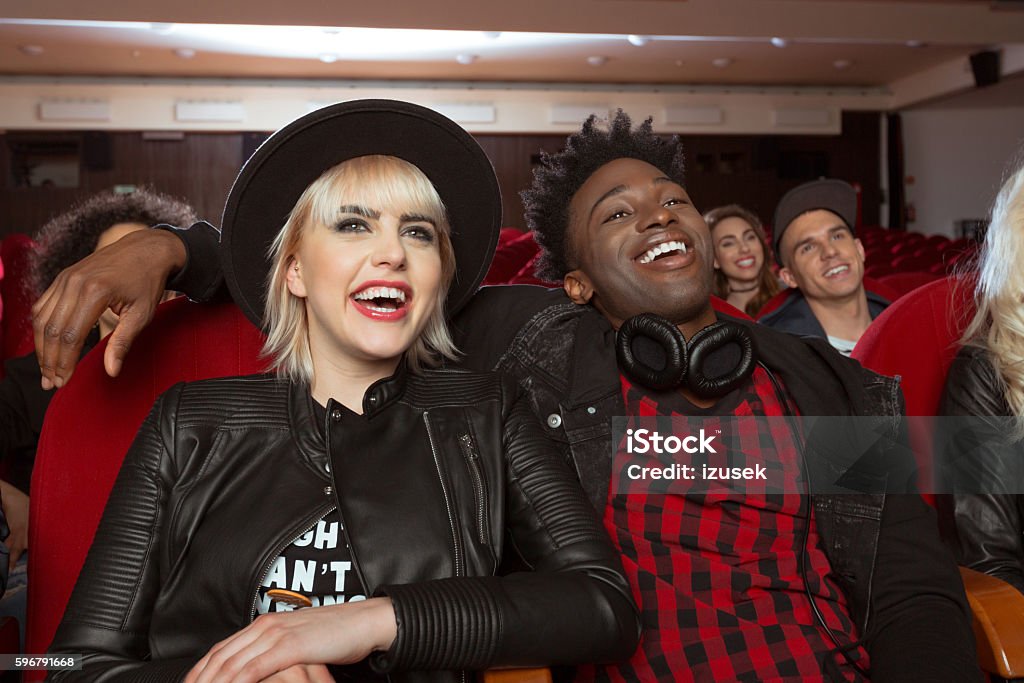 Multi ethnic young couple in the movie theater Multi ethnic group of young people in the movie theater, watching comedy. Close up of blonde young woman and her afro american boyfriend. Adult Stock Photo