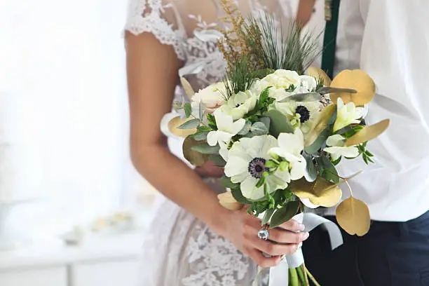Bride holding wedding bouquet with ranunculus, freesia, roses and white anemone