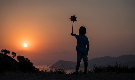 Rear view of Boy holding a toy windmill at sunrise, horizontal composition