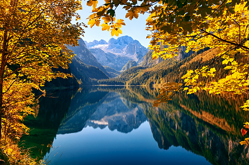 Autumn forest surrounding the lake in hilly countryside landscape. Tranquil moment - no waves on the water surface.