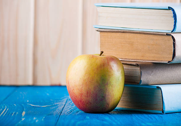 istock Stack of books and apple on a blue wooden shelf 596799080