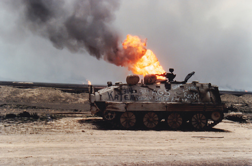 Kuwait City, Kuwait - April 1, 1991: Damaged tank on road with burning oil fire from Persian Gulf War.