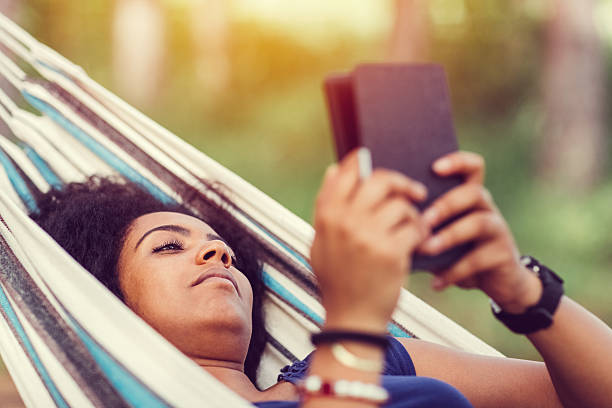 Weekend activities among nature Young girl reading e-book in a hammock hammock relaxation women front or back yard stock pictures, royalty-free photos & images