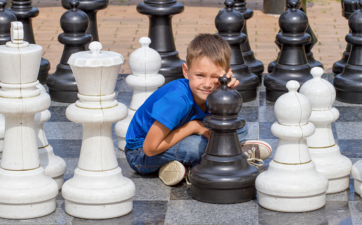Smiling boy sitting on outdoor chess game board in the park