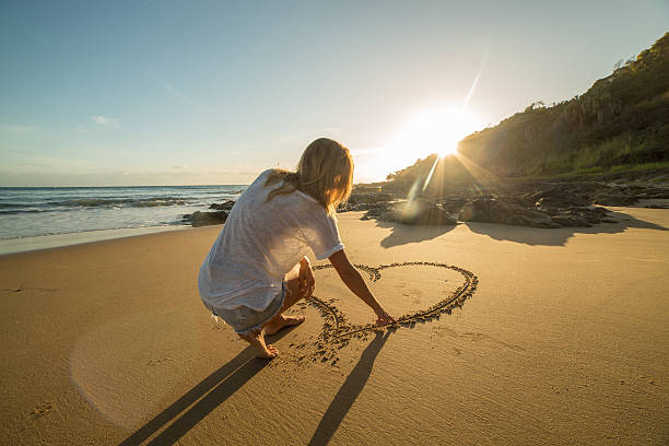 istock Female drawing heart shape on beach at sunrise 597211544