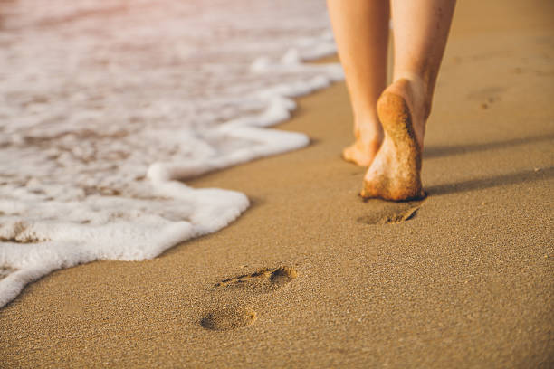 frau zu fuß auf sandstrand hinterlässt fußabdrücke im sand - footprint sand sea beach stock-fotos und bilder