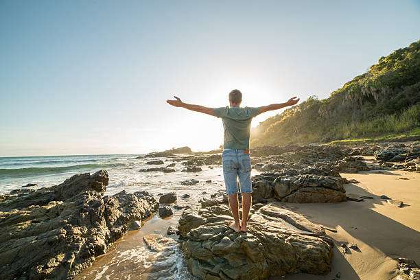 istock Young man arms outstretched on the beach at sunrise 597222900