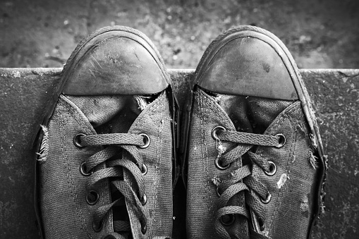 Pair of old sneakers standing on concrete stairs, closeup top view. Black and white retro stylized photo
