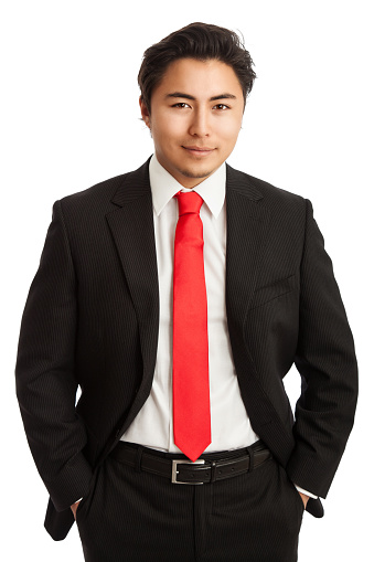 Attractive businessman in a black suit with a red tie looking at camera standing against a white background.