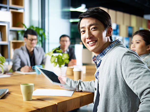 young asian businessman looking at camera young confident asian businessman turning to look at camera during meeting in office. founder stock pictures, royalty-free photos & images