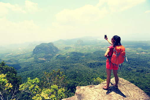young woman hiker taking photo with smartphone on mountain peak cliff