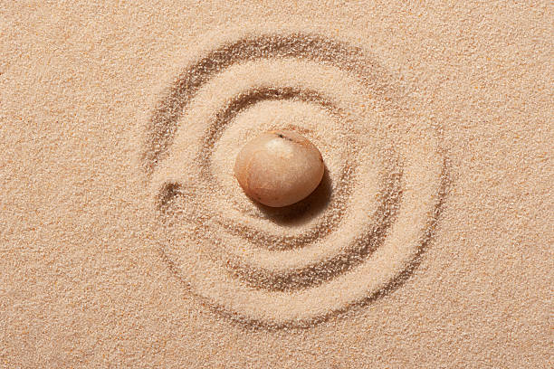 istock Spiral drawn on beach sand with pink round sea stone 597250498