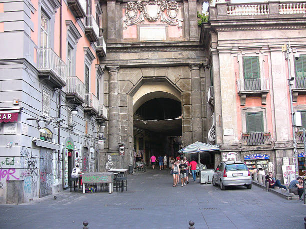 Naples, Italy - August 27, 2016: the ancient gateway, called Port'Alba, to another part of the century city, on the corner of Dante square. Recognizable people and shop signs at a distance, a blurred plate of one car.
