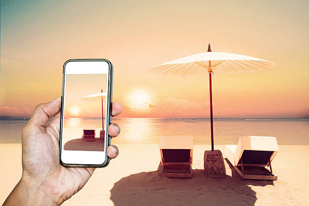 istock Hand holding smart phone, withTropical beach in sunset 597253842