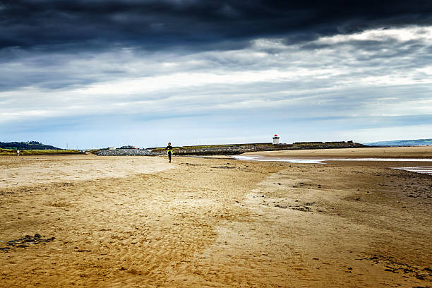 зрелая женщина бег трусцой на пляже белый маяк в фоновом режиме - wales beach editorial people стоковые фото и изображен�ия
