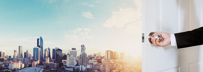 Businessman hand holding door knob opening, with Bangkok cityscape in sunrise