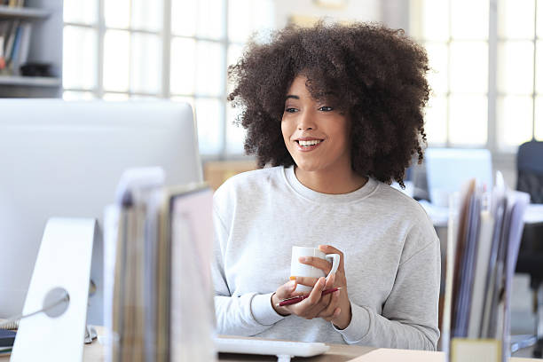 istock Smiling young woman drinking coffee at workplace 597263354