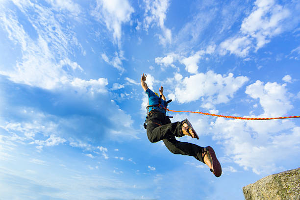 Jump rope from a high rock in the mountains. The first jump off the cliff with a safety rope. bungee jumping stock pictures, royalty-free photos & images