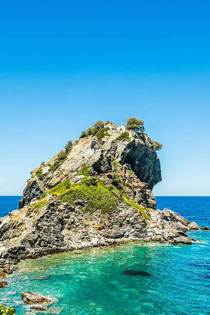 Rock with famous church Agios Ioannis Kastri on Skopelos island, Greece, where scenes of Mamma Mia! movie were filmed. Sun raises above Alonissos island.