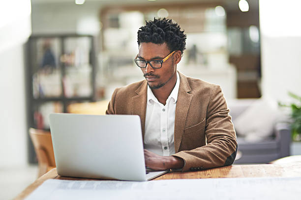 Data management has always been his forte Cropped shot of a young businessman working on his laptop at his desk in his office black man laptop stock pictures, royalty-free photos & images