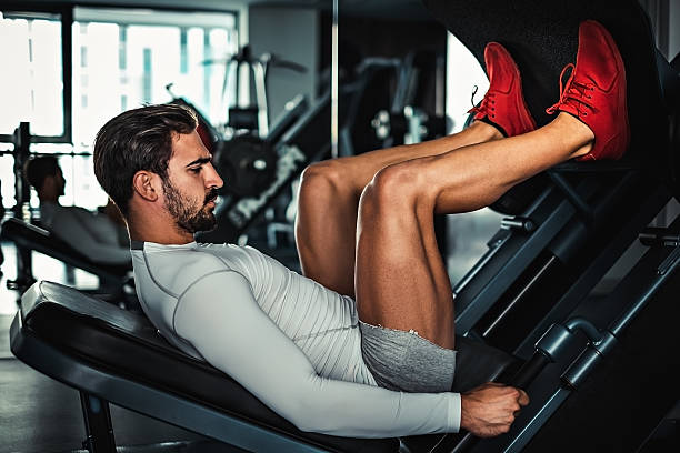 hombre centrado en el entrenamiento de piernas en la máquina - máquinas de ejercicios fotografías e imágenes de stock