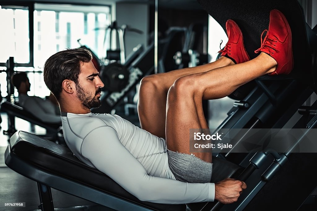 Man focused on training legs on the machine Man focused on training legs on the machine in the gym Leg Press Stock Photo