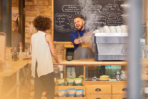 a coffee shop barista chats to his customer as he prepares her order.