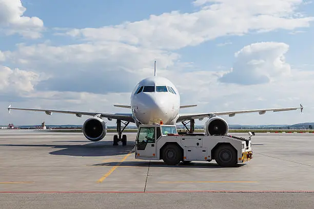Photo of Vehicles towing white modern aircraft on parking lot